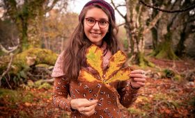 Woman standing among trees. holding a chestnut leaf in her hands
