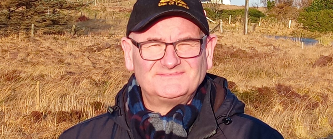 man on a road wearing a black cap and black coat, he is wearing glasses