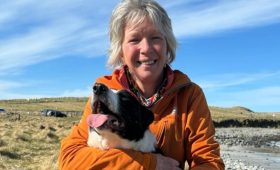 woman with white hair, wearing a orange top and holding a border collier dog
